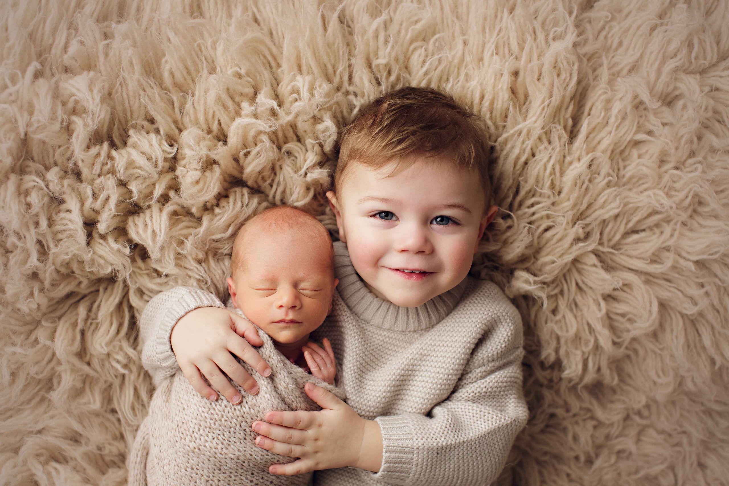 Older sibling cuddling a newborn baby during a professional newborn photography session