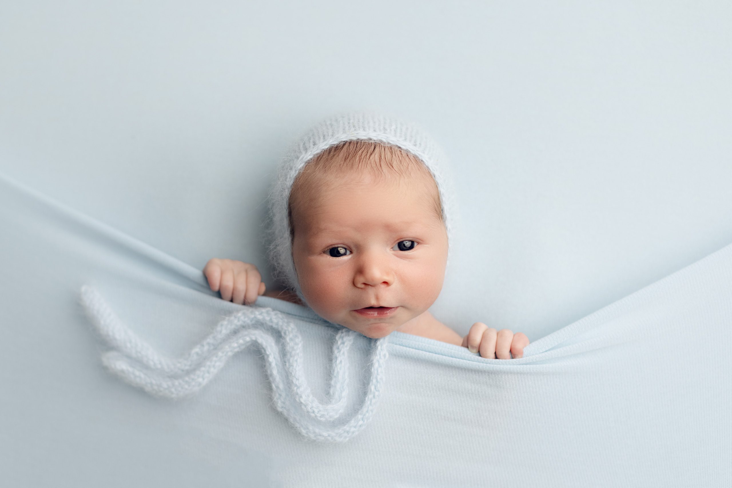 Newborn baby peeking over a soft blue wrap during a studio newborn session