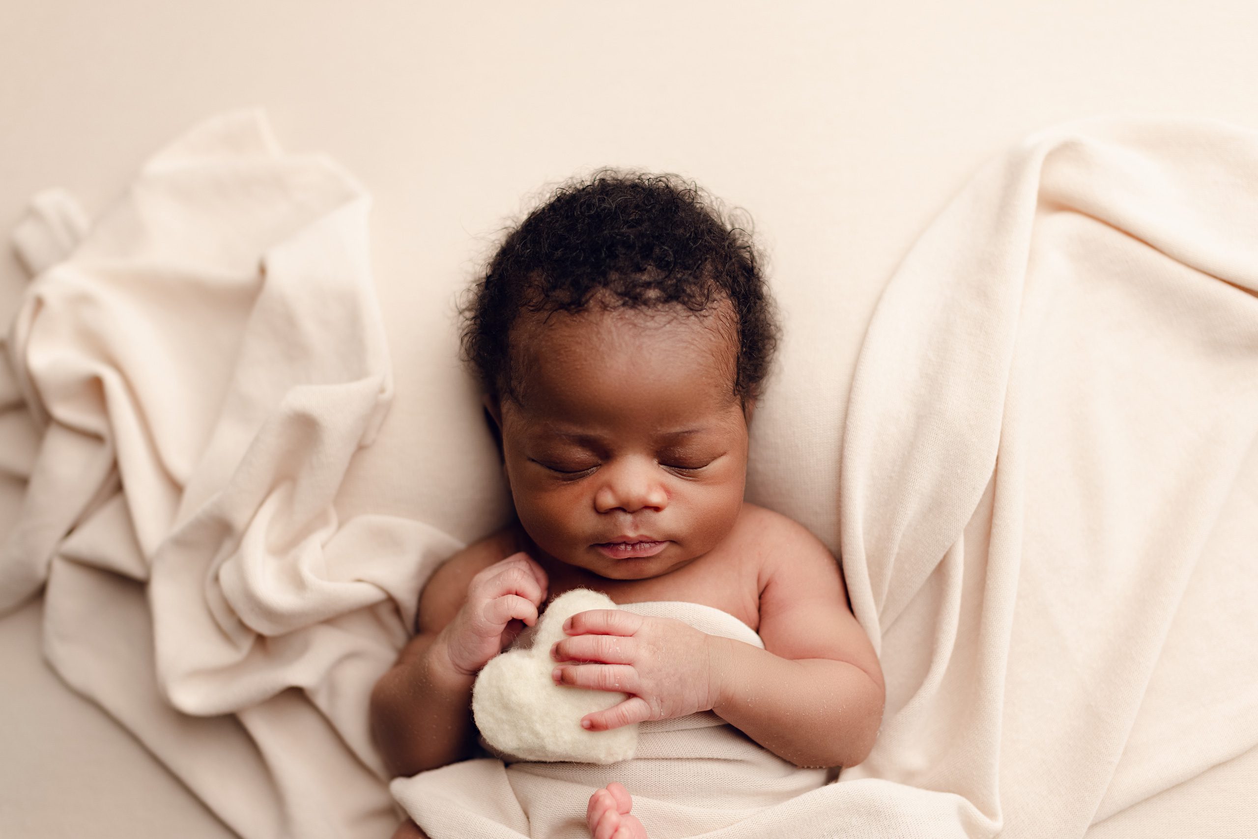 Newborn baby resting peacefully on soft cream fabric.