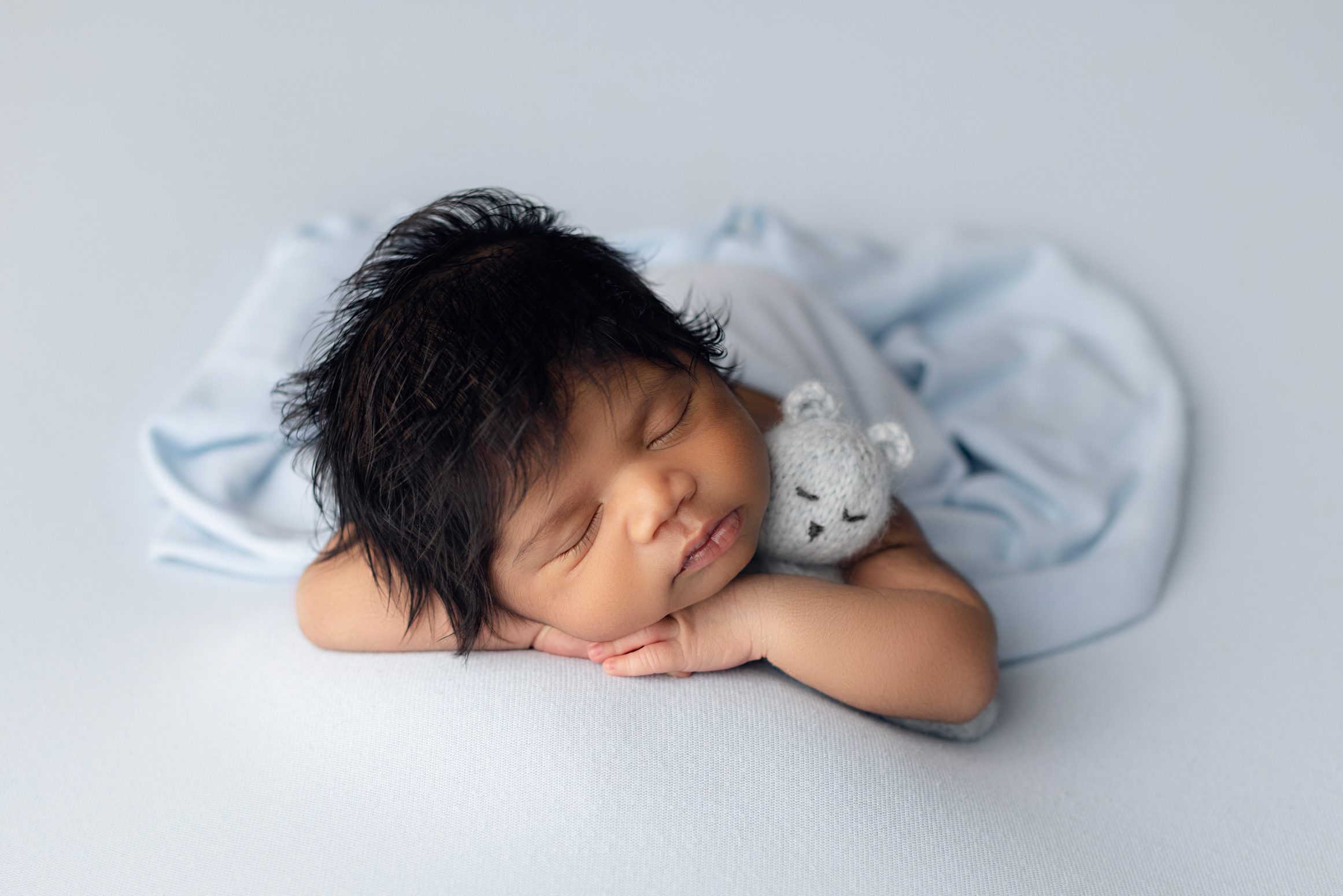 Sleeping newborn baby posed on a light blue backdrop.