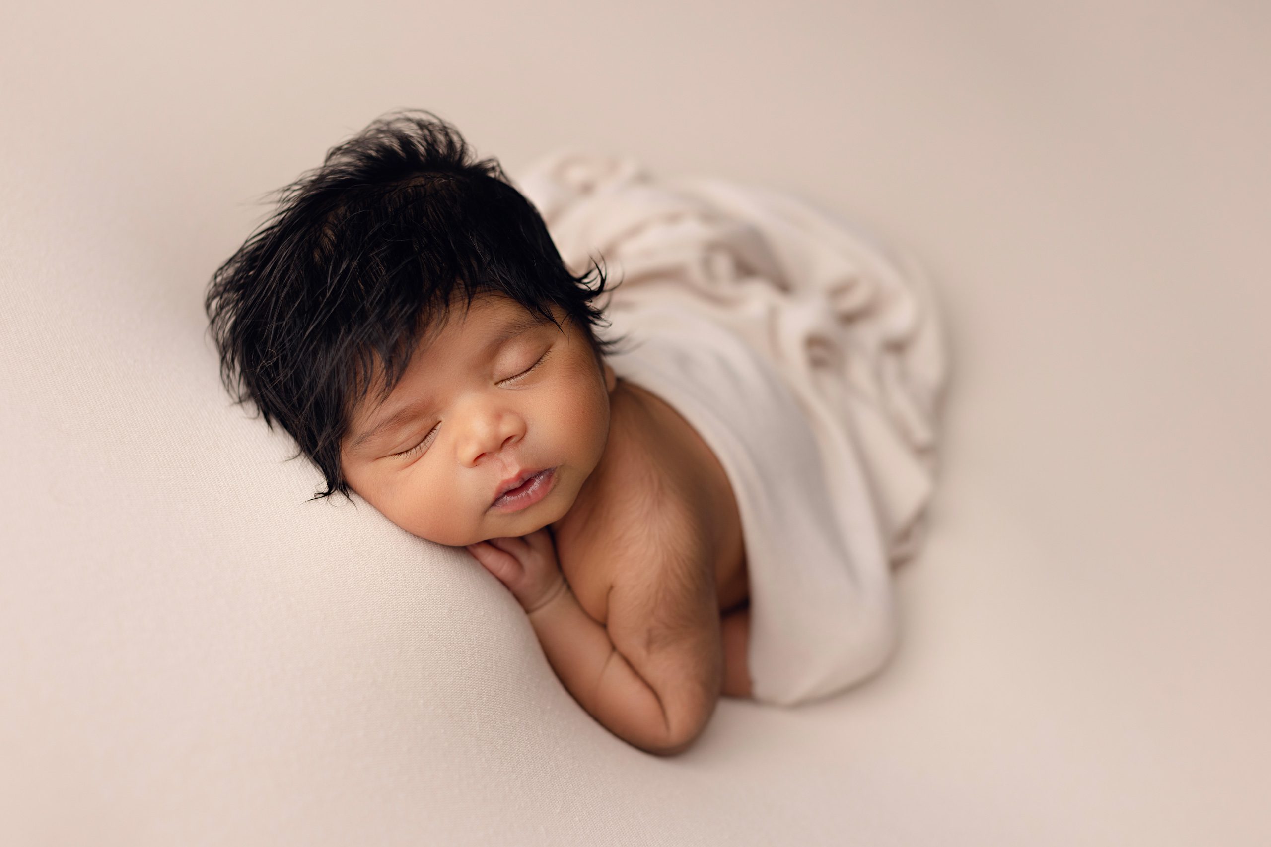 Sleeping newborn baby in a soft cream wrap photographed during a natural newborn photography session in Minnesota.