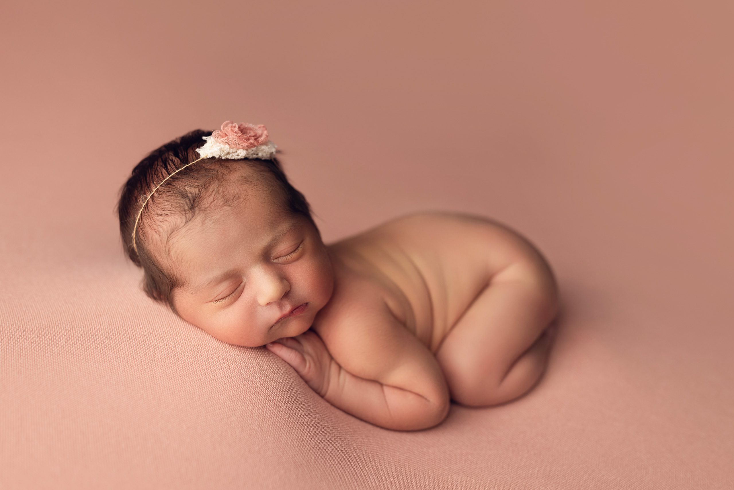 Newborn baby posed on soft pink fabric.
