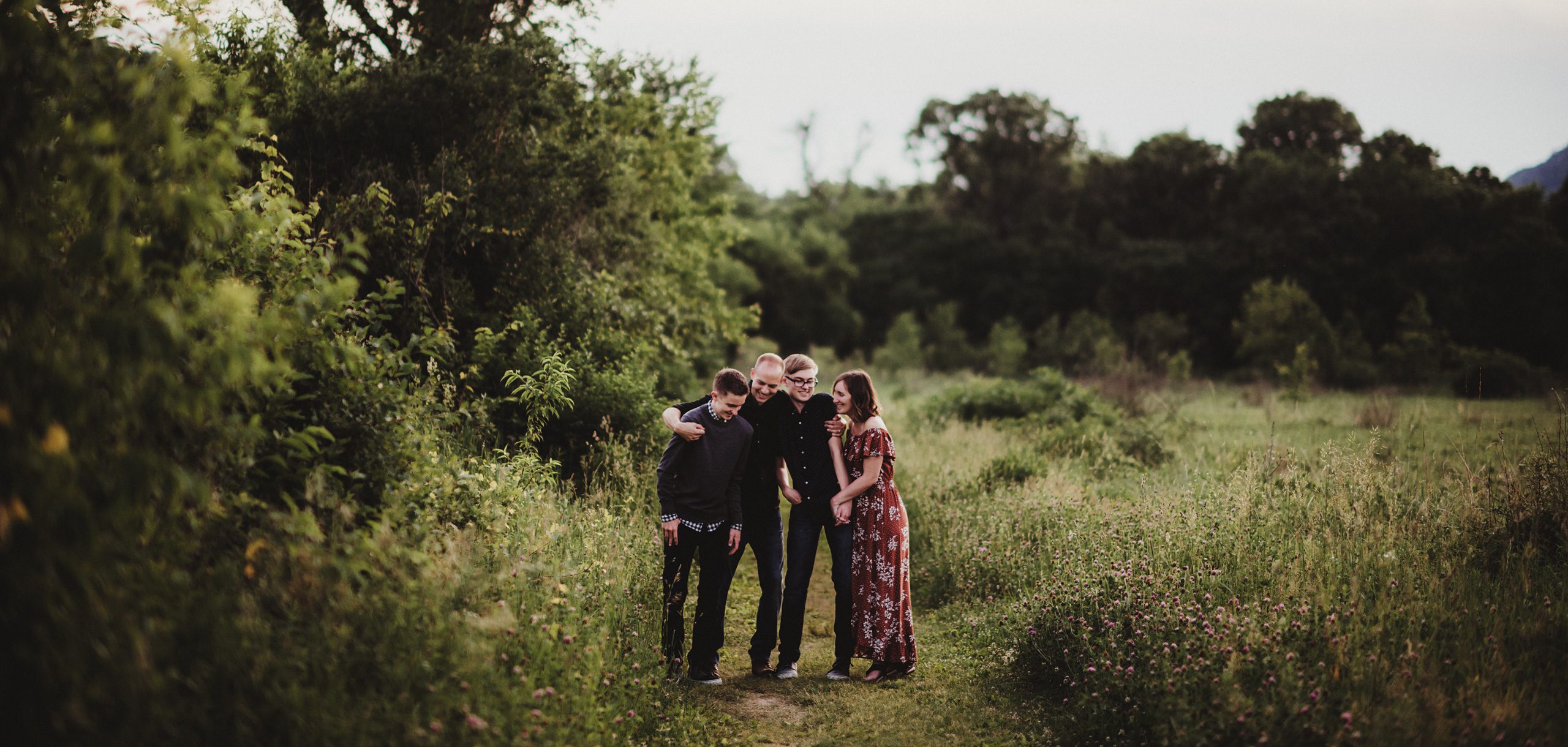 Rebecca Cramer, owner of Tiny Me Photography, walking with her husband and two sons in a peaceful field.